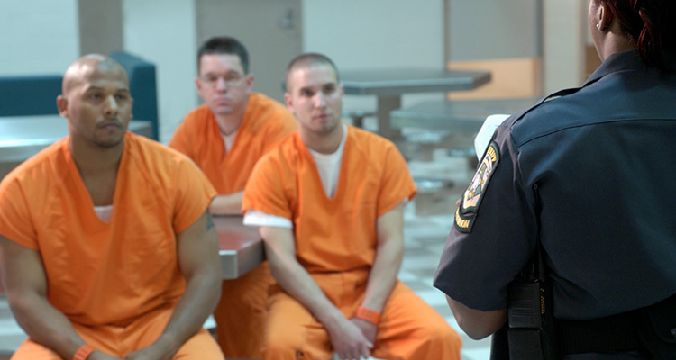 Three male inmates wearing orange receiving instructions from a prison guard.