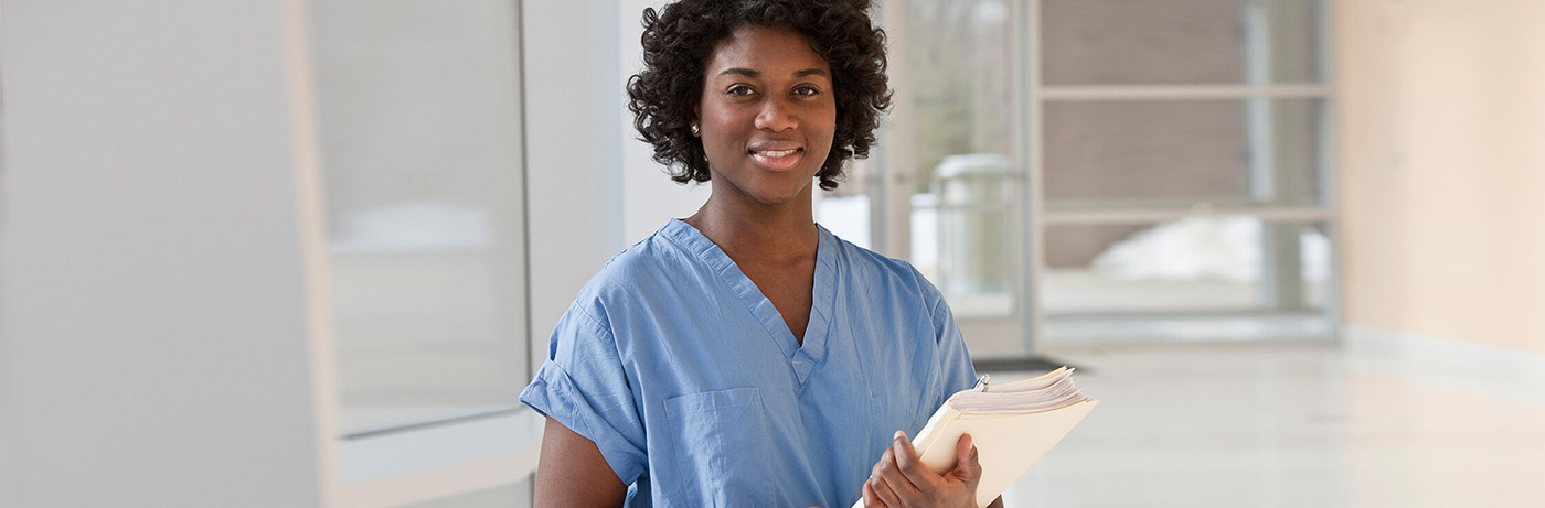 Young female nurse in scrubs stands holding a large patient file.