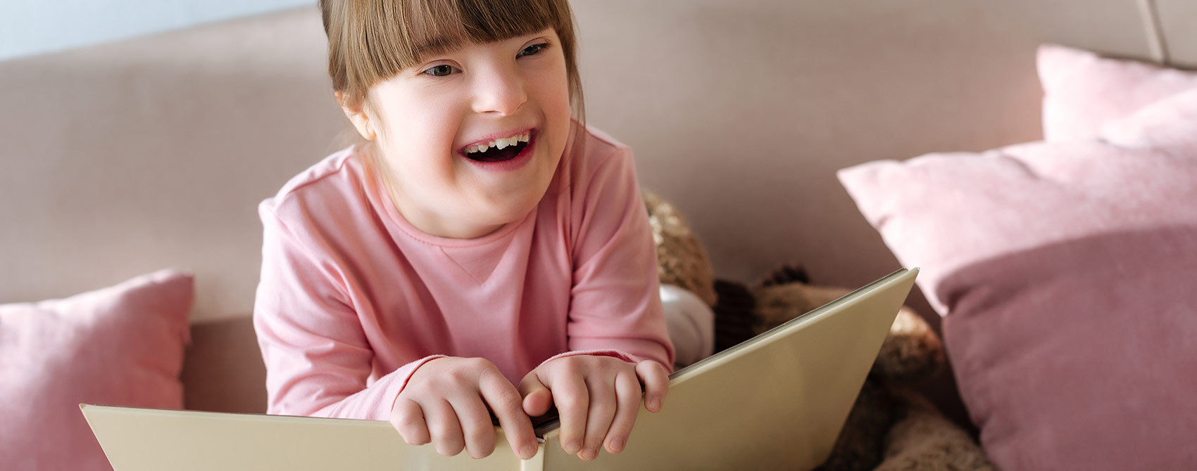 A smiling young girl with special needs holds an open book.