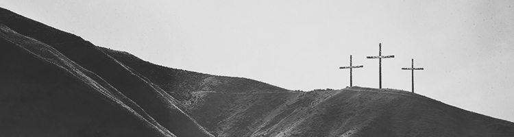 Three wooden crosses on a grassy hill photographed in black and white.