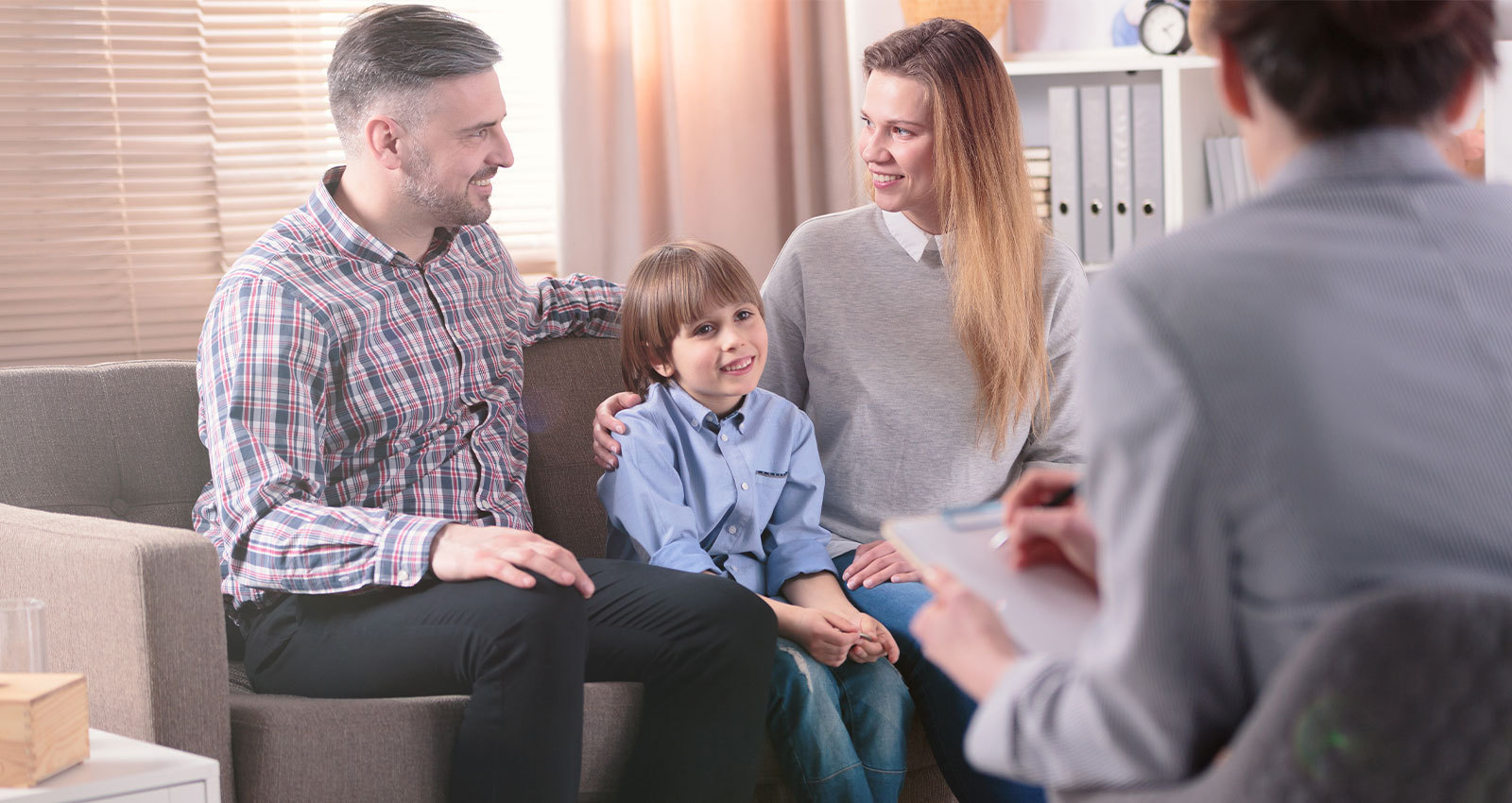 Smiling foster family, two parents and child, sitting with a social worker.