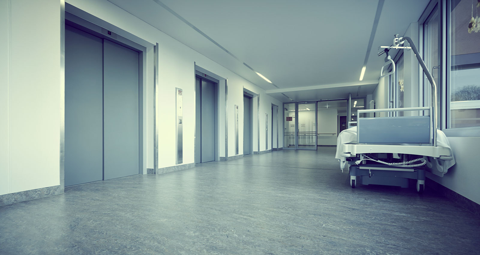 Empty hospital corridor with unoccupied bed and elevators.