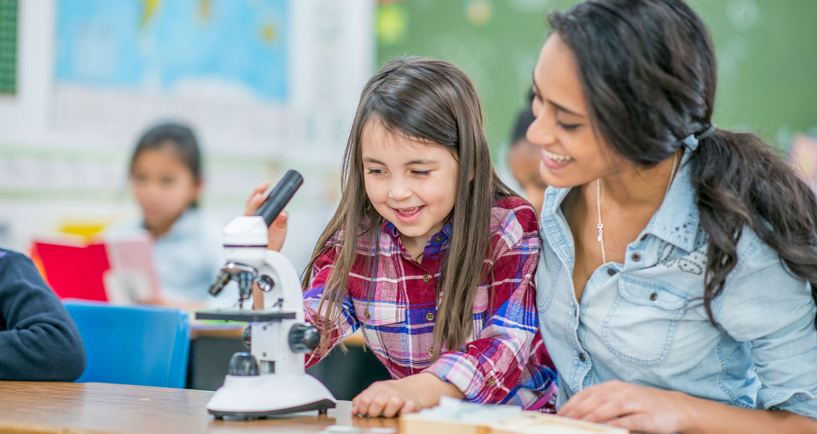 Teacher encourages young female student using a microscope.