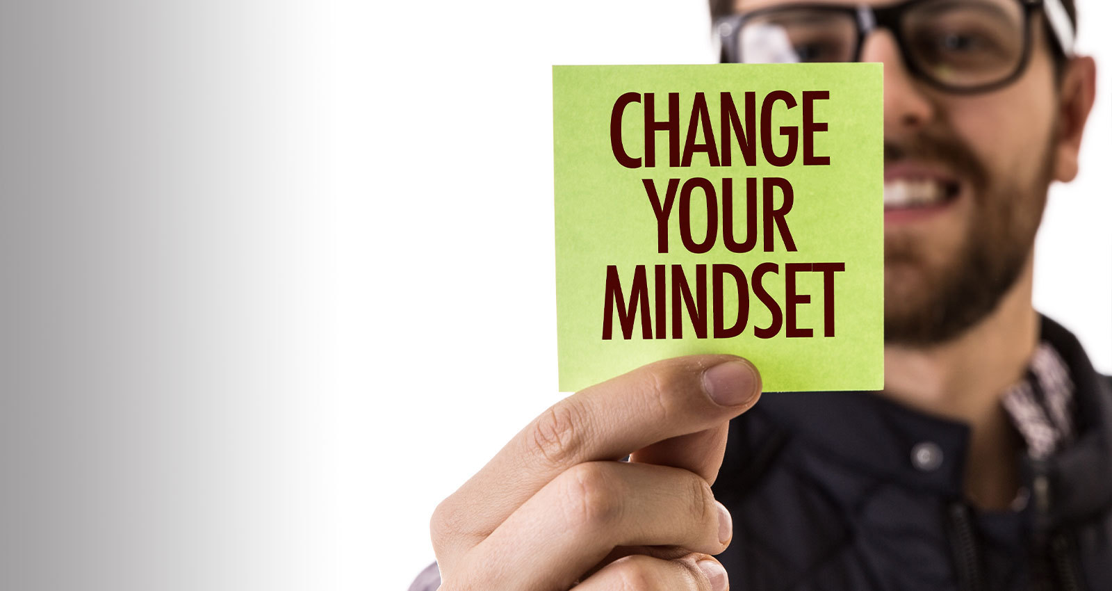 Smiling man with glasses and beard holds a yellow card that reads "change your mindset".