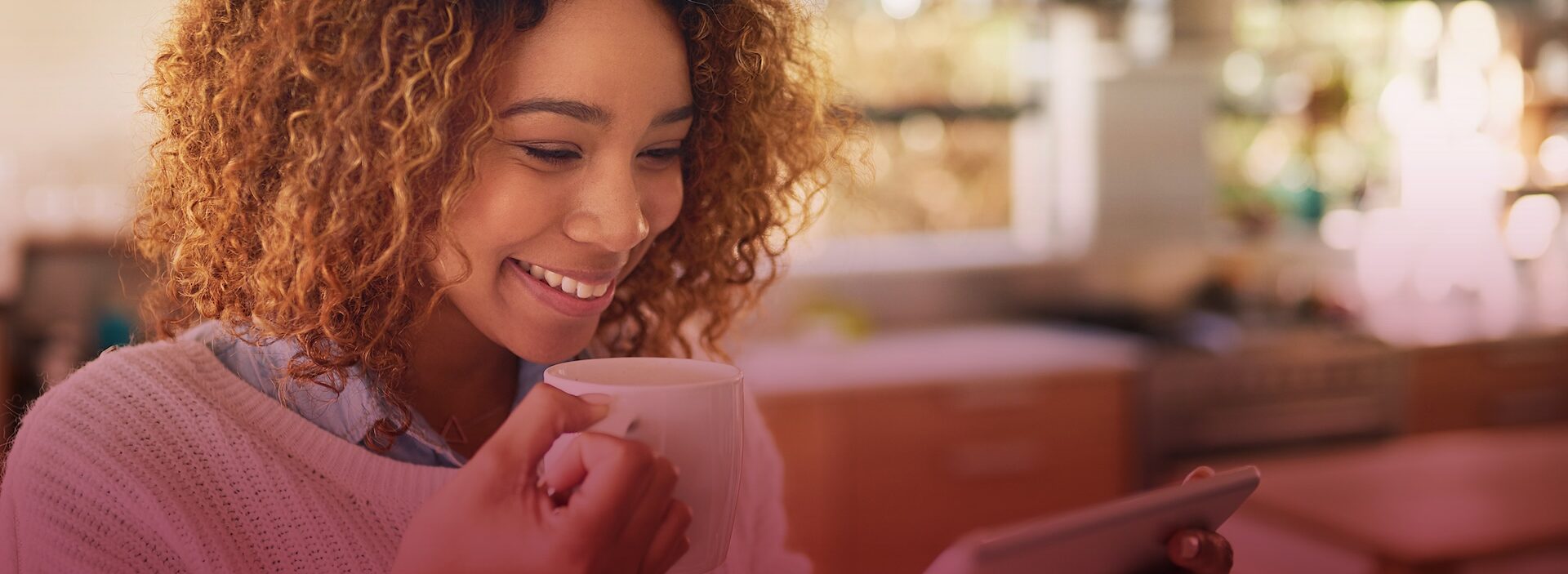 woman holding a coffee mug and smiling while looking at tablet