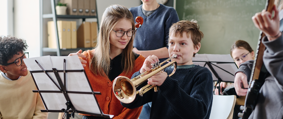 Students playing trumpet, violin, and guitar together in school music ensemble class