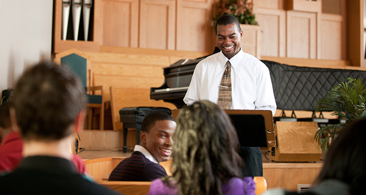 Young man ministers to his congregation in a church with pews and a piano.