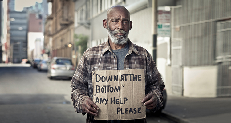 Photo of homeless African American man in a gentrified neighborhood holding a cardboard sign.