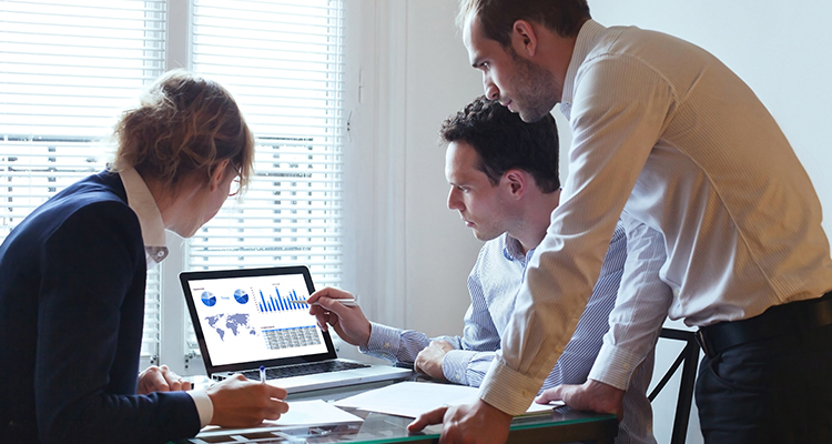 Three co-workers, one female and two males, studying financial graphs on a laptop.