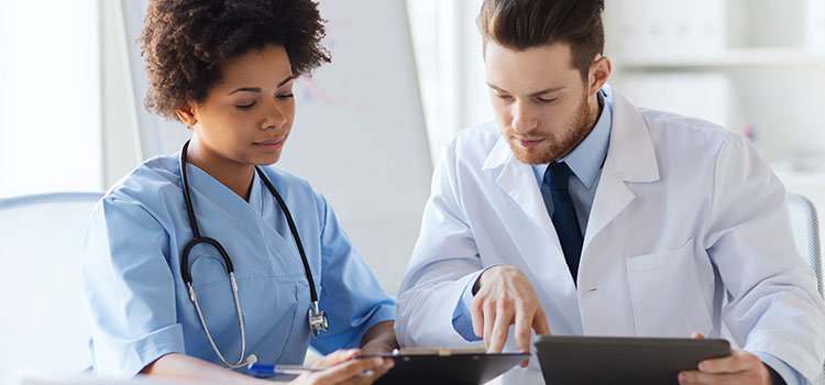 Female nurse in blue scrubs discussing patient chart with male doctor in white coat.